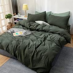 an unmade bed with green comforter and pillows on top of it in front of a window