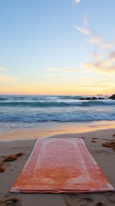 an orange rug is laying on the sand at the beach as the sun goes down