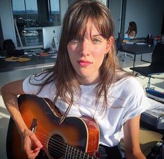 a young woman holding an acoustic guitar in front of her face and looking at the camera