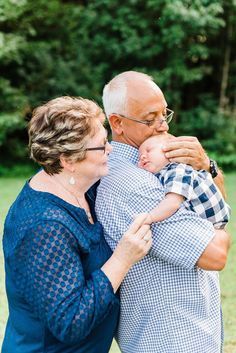 an older man holding a baby in his arms while standing next to a woman with glasses