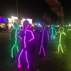 many people are standing in the dark with neon lights on their body and arms,