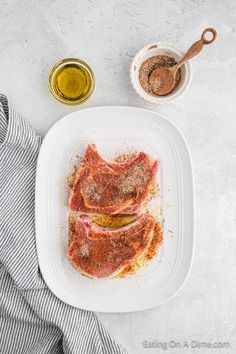 two pieces of meat on a plate with spices and seasoning next to it,