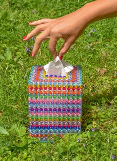 a woman's hand reaching for a tissue paper in a colorful box on the grass