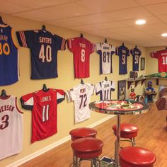 sports jerseys are hung up on the wall in this room with stools and tables