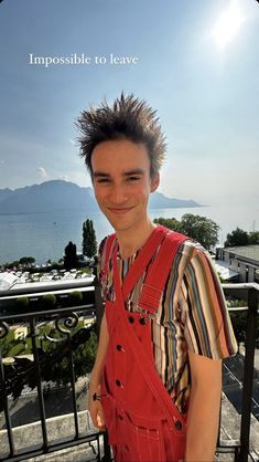 a young man with spiked hair and overalls standing on a balcony overlooking the ocean