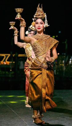 a woman is dressed in an elaborate costume and holding two golden candles on her arm