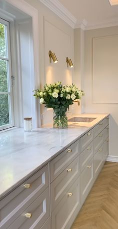 a vase with white flowers sitting on top of a kitchen counter next to a window