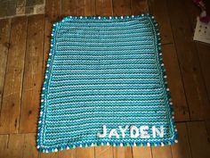 a crocheted blanket with the name jayden on it sitting on a wooden floor