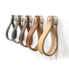 four different colored leather handles hanging on a white wall with metal hooks in the shape of an o - ring