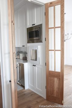 an open door leading to a kitchen with white cabinets and stainless steel appliances in it