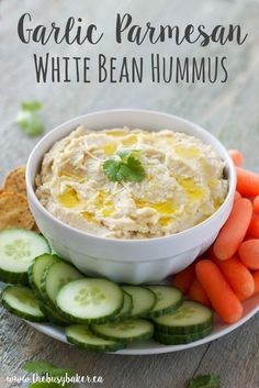 a bowl of hummus, carrots and cucumbers on a plate with crackers