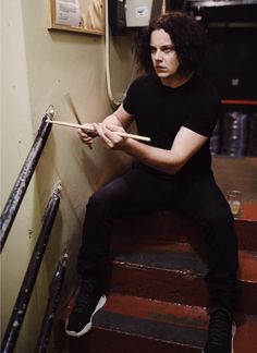 a man with long hair sitting on some stairs holding a stick and looking at the camera