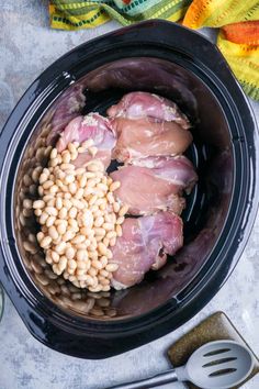 three pieces of meat in a slow cooker with beans and seasoning on the side