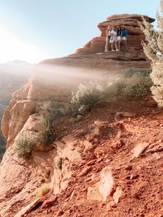 three people standing on the edge of a cliff with mist coming out of the top