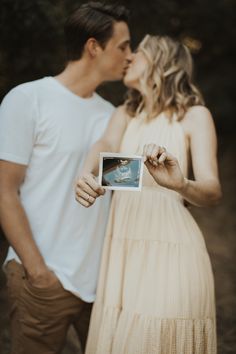 a man and woman kissing while holding up a polaroid