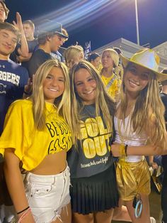 three girls in yellow shirts and white shorts posing for the camera at a football game