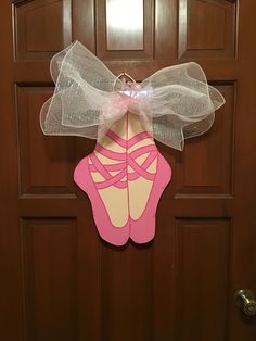 a door hanger with a pink ballerina shoe on it's side and a white bow