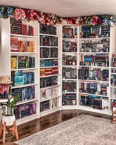 a living room filled with lots of books on top of a white book shelf next to a chair