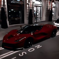 a red sports car is parked in front of a building with people walking around it