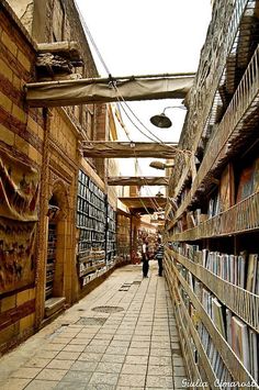 two people are walking down an alley way with books on the shelves in front of them