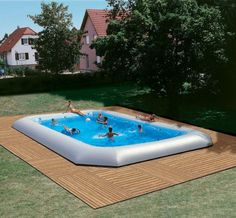 an inflatable pool with people playing around it on the grass near some houses