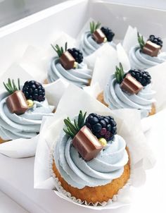 some cupcakes with white frosting and blackberries on top are in a box