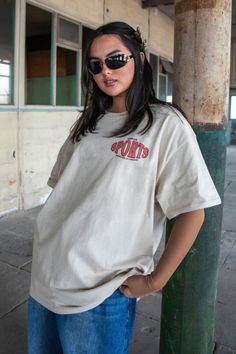 a woman wearing sunglasses and a t - shirt Relaxed Fit Graphic Print T-shirt Athleisure, Sporty T-shirt With Front Print For Streetwear, Casual T-shirt With Front Print For Sports Events, Summer Sports T-shirt With Screen Print, Sporty Cotton T-shirt With Front Print, Sporty T-shirt With Front Print And Relaxed Fit, Cotton Short Sleeve T-shirt For Sports Season, Sporty Screen Print T-shirt For Streetwear, Relaxed Fit Sports T-shirt With Text Print