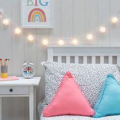 a white bed topped with lots of pillows next to a night stand and lights on the wall