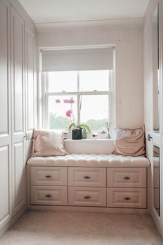 a window seat with drawers underneath it in a white room next to a window filled with pink flowers