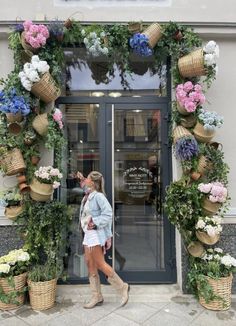 a woman standing in front of a building with flowers and baskets on the entrance door