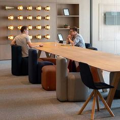 two people sitting at a table with laptops on it in an open office space