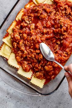 a person holding a spoon over a casserole dish filled with meat and cheese