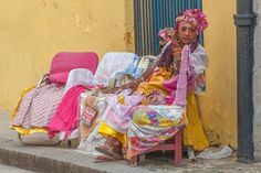 a woman sitting on a chair in front of a yellow building with lots of clothes