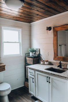 a bathroom with wood plank ceilings and white cabinets, including a sink in the center