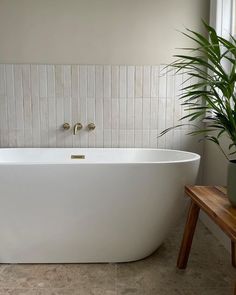 a large white bath tub sitting next to a wooden table with a potted plant