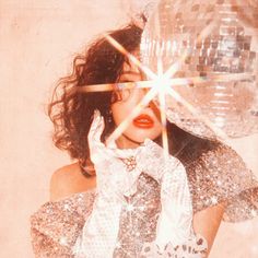 a woman with shiny clothes and a disco ball in the background is holding her hands up to her face