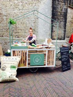 an outdoor food cart is set up on the side of a brick road with two people sitting at it