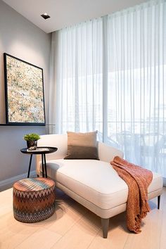 a white couch sitting next to a table with a vase on top of it in front of a window