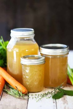 three jars filled with liquid next to carrots and celery on a table