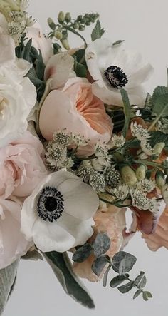 an arrangement of flowers in a vase on a white table top with greenery and leaves