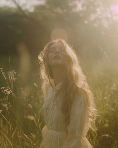 a woman standing in tall grass with her eyes closed and the sun shining behind her