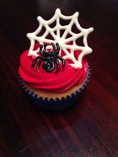 a cupcake decorated with spider webs and red icing on a wooden table