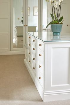 a vase with flowers on top of a white cabinet in a room that has beige carpet