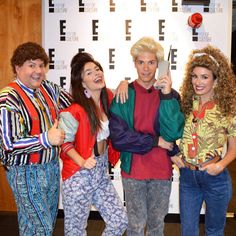 four people standing in front of a wall holding scissors