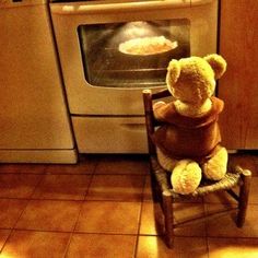 a teddy bear sitting on a chair in front of an oven with food cooking inside