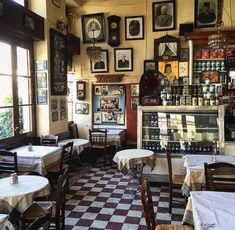 the interior of a restaurant with tables and chairs covered in white tablecloths, framed pictures on the wall