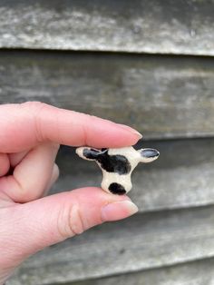 a hand holding a tiny black and white cow figurine