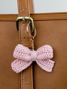 a pink crocheted bow hangs from the handle of a brown purse