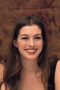 a woman with long brown hair smiling at the camera, wearing a black dress and diamond necklace