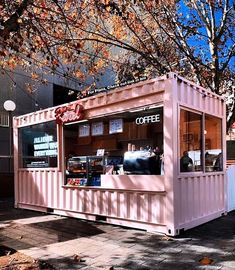 a pink coffee shop sitting on the side of a road next to a tree with lots of leaves